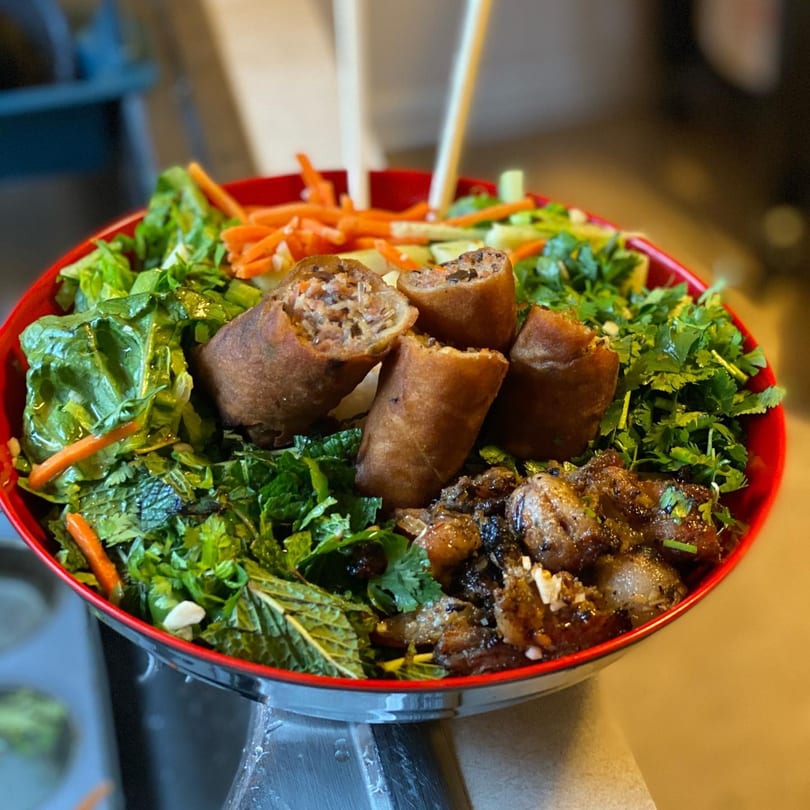 A vibrant Simply Boba Vietnamese vermicelli bowl with spring rolls, grilled meat, and fresh greens.