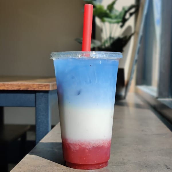 A Simply Boba drink with red, white, and blue layers, and a red straw, on a counter.